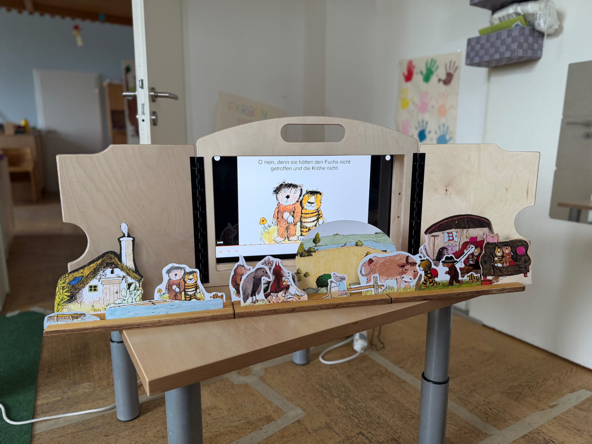 eKami mit einer Onilo Boardstory: Auf dem Bildschirm läuft ein animierter Bilderbuchklassiker, vor der Bühne stehen passende haptische Figuren auf der Erzählschiene.